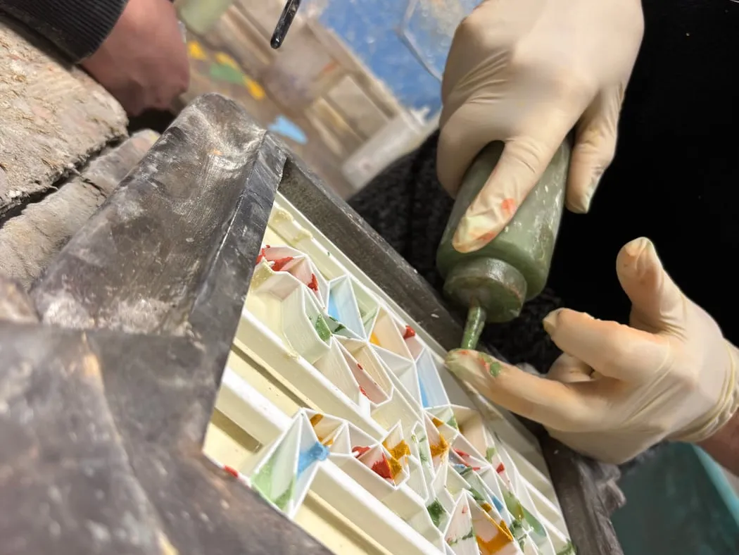 Gloved hands pouring coloured pigment into a tile mould
