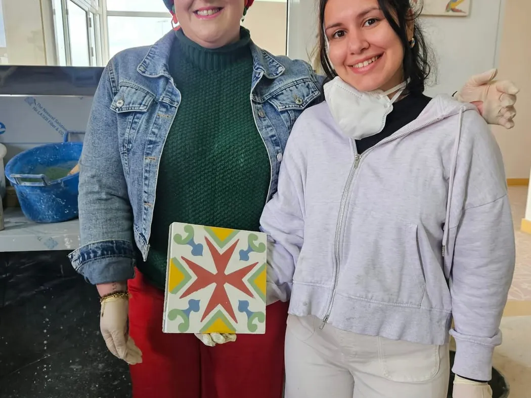 Two visitors holding the star-patterned tile they made